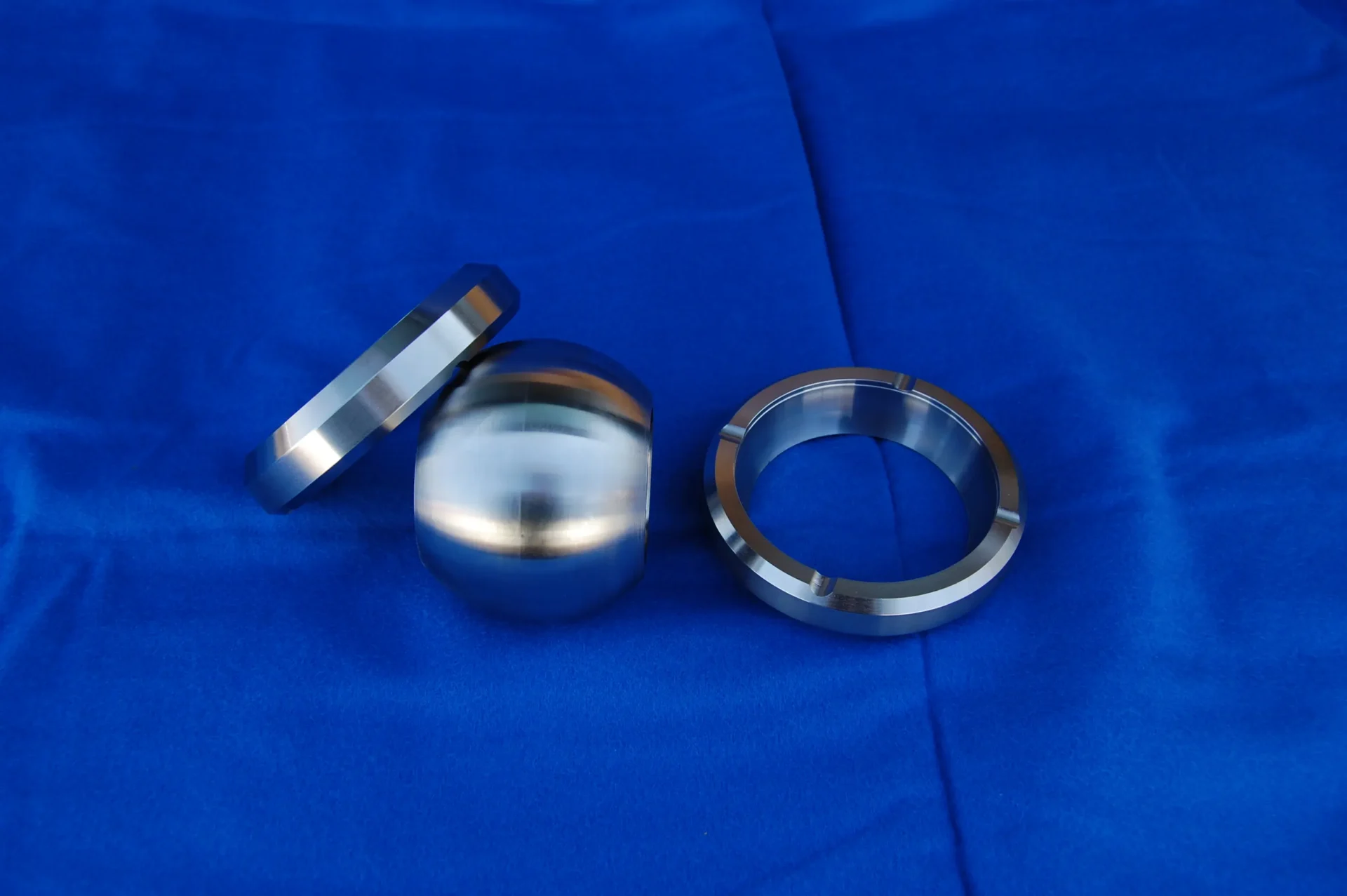 Three metallic spherical parts on a blue fabric background.