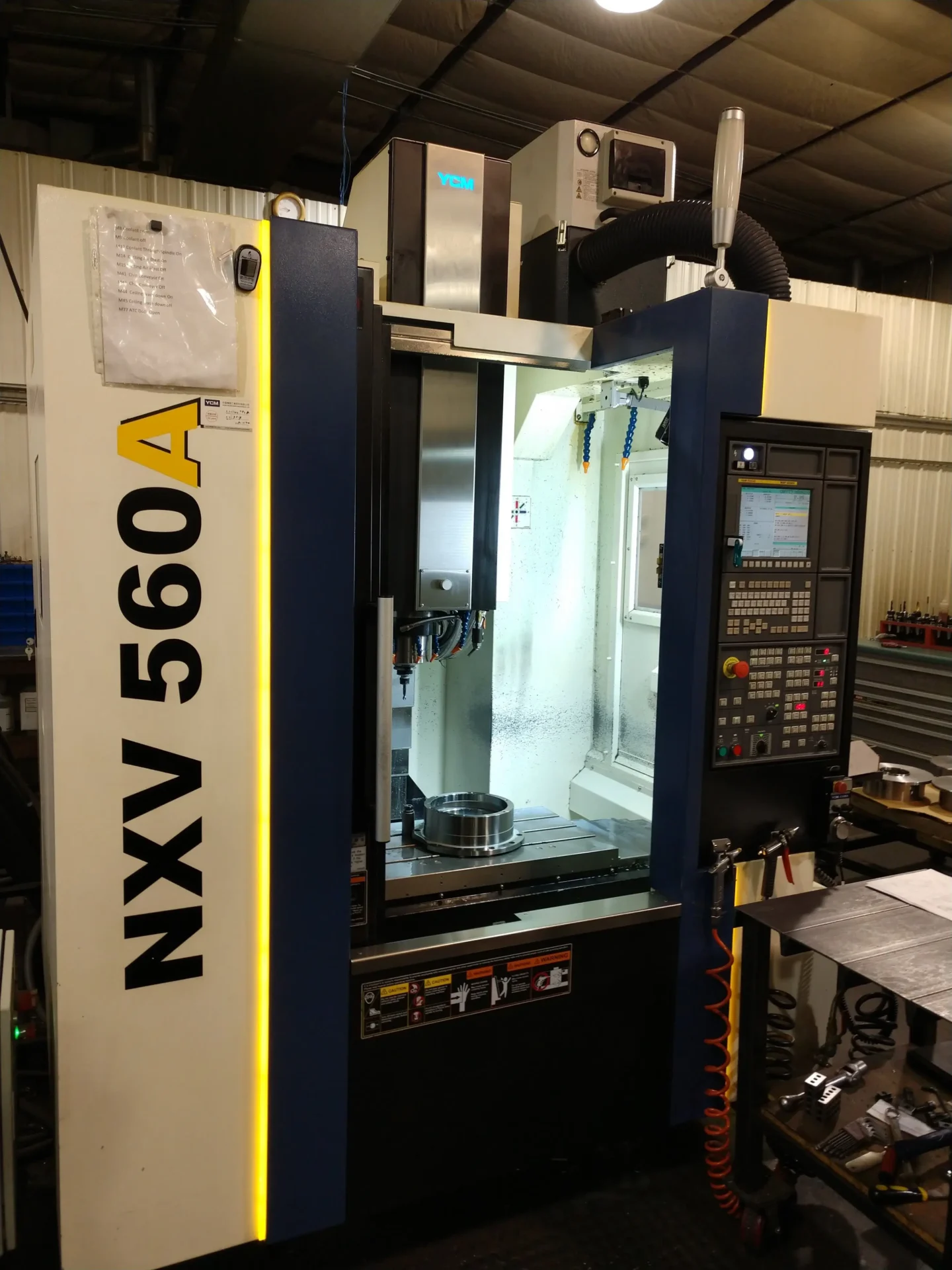 The NXV 560A CNC machine with its door open, showing the illuminated workspace inside.